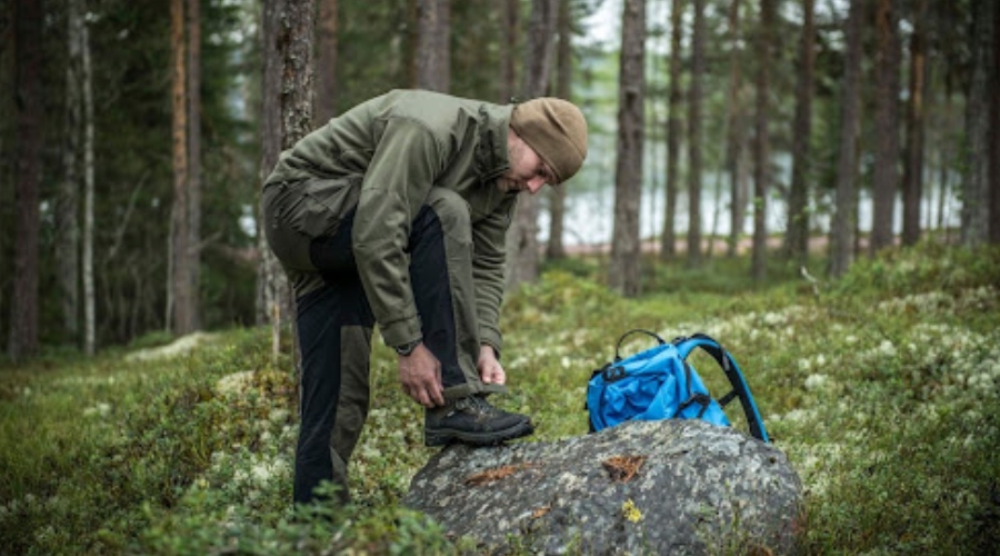 Muž v outdoorovém oblečení v lese s batohem. 