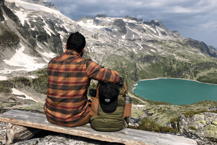Muž s batohem sedí na horách a dívá se na jezero.
