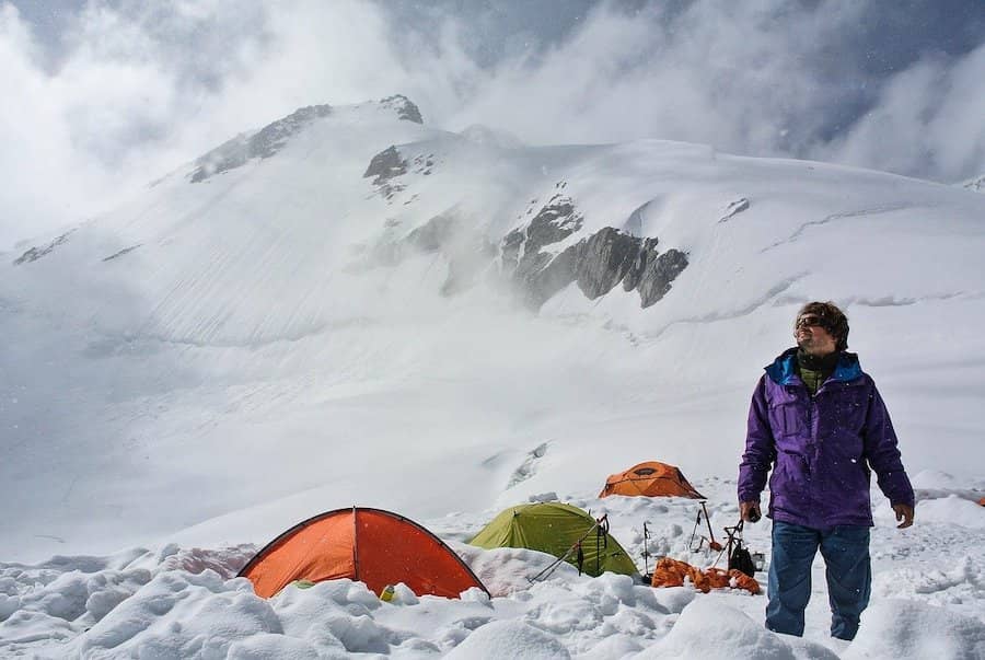 Muž stojící vedle stanů ve sněhu v horách